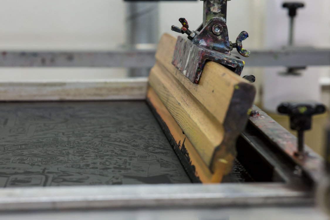 A squeegee presses inks through a screen mesh.